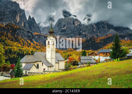 Stunning autumn mountain scenery with cute church in the fabulous alpine village, Colfosco, Dolomites, Italy, Europe