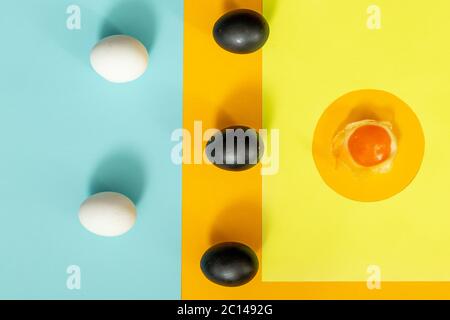 Two white eggs with three black eggs and a crashed egg on a yellow with blue background. Stock Photo