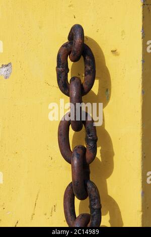 rusty metal chain hanging on yellow concrete pedestal and casts a shadow. Stock Photo