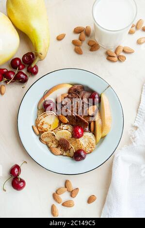 trending food cereal pancakes. small pancakes with fresh pears, cherries, almonds in a metal blue plate on the background of the kitchen table with fr Stock Photo