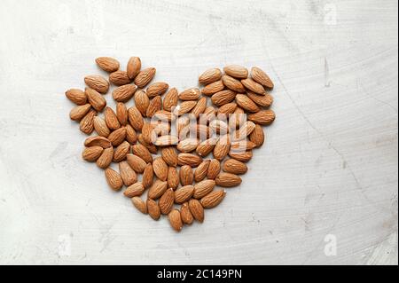 almonds nut laid out in the shape of a heart on a light concrete surface, top view, photo of food content Stock Photo