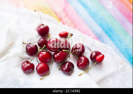 ripe juicy red cherries in drops of clear water on white cotton napkin on bright multi-colored wooden cover Stock Photo