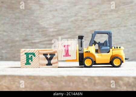 Toy forklift hold letter block I to complete word FYI (Abbreviation of For your information) on wood background Stock Photo