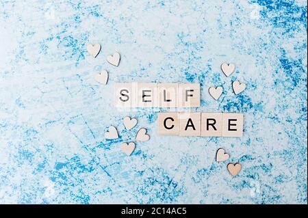 self care lettering in square wooden letters with small wooden hearts on a blue and grey concrete background. layout about Taking care of yourself and Stock Photo