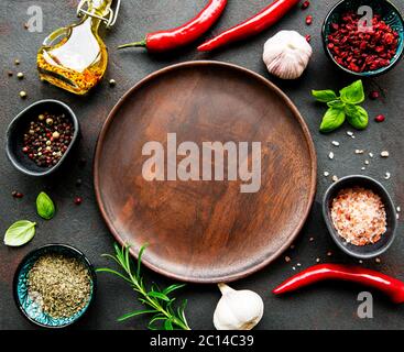 Empty wooden plate and frame of spices, herbs and vegetables on a dark stone background. Top view, flat lay. Stock Photo