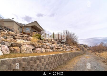 Dirt road along homes on a slope with huge rocks and concrete retaining wall Stock Photo