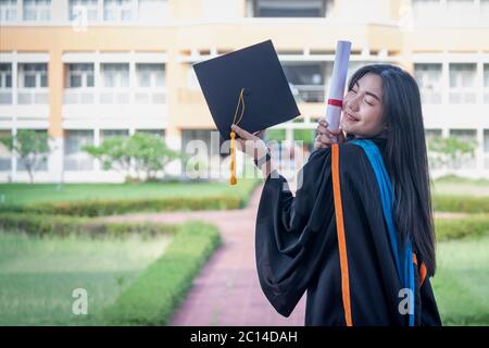 Portrait of happy and excited of young Asian female university graduate wears graduation gown and hat celebrates with degree in university campus Stock Photo