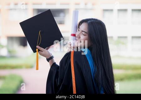 Portrait of happy and excited of young Asian female university graduate wears graduation gown and hat celebrates with degree in university campus Stock Photo