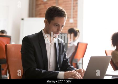 Focused employee intern using laptop, working on online project Stock Photo