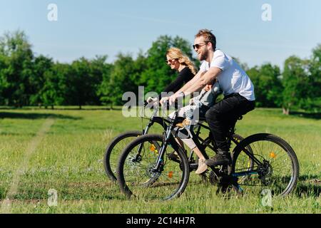 Cheerful family riding along sunlit trees and fields Stock Photo