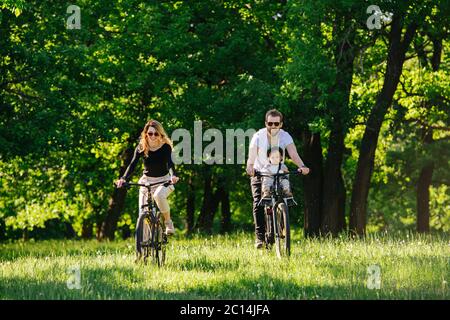 Mom, dad and their jolly son biking on grass through wood opening Stock Photo