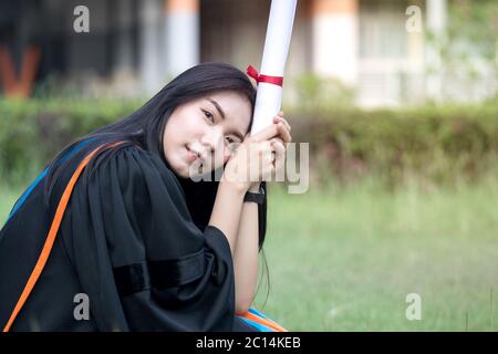 Portrait of happy and excited of young Asian female university graduate wears graduation gown and hat celebrates with degree in university campus Stock Photo