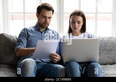 Serious young couple checking financial documents, using online banking service Stock Photo