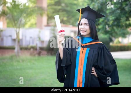 Portrait of happy and excited of young Asian female university graduate wears graduation gown and hat celebrates with degree in university campus Stock Photo