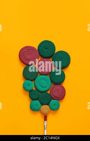 Paint brush and rolls of fabric stripes on an orange background. The fabric stripes are made of old wears. The concept of upcycling and zero waste. Stock Photo