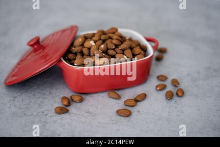 Almonds in red porcelain bowl on wooden table. Almond concept with copyspace. Stock Photo