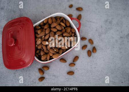 Almonds in red porcelain bowl on wooden table. Almond concept with copyspace. Stock Photo