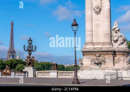 France. Summer sunny day in Paris. Historic column and lanterns on the bridge Alexandre III across the river Seine. Eiffel Tower in the distance