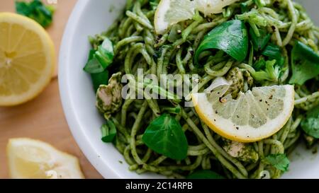 Vegan pasta with avocado dip sauce, spinach leaves and lemon in white bowl plate. On wooden background. Vegetarian healthy food Stock Photo