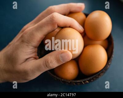 Person choosing the best egg from bowl of raw chicken eggs on the wooden background. Space for text Stock Photo
