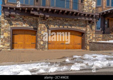 facade of home featuring two hinged wooden garage doors and stone brick wall Stock Photo