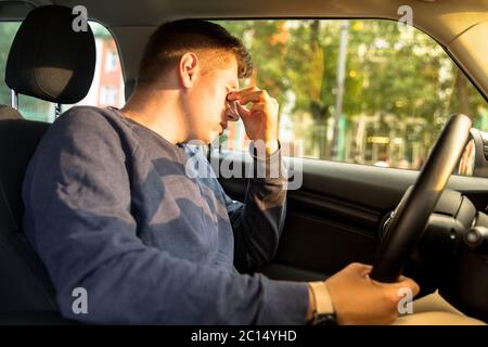 Young Caucasian driver falling asleep sitting inside her car, rubbing eyes, stopped to rest. Tired man having headache after driving. Exhausted, sleep Stock Photo