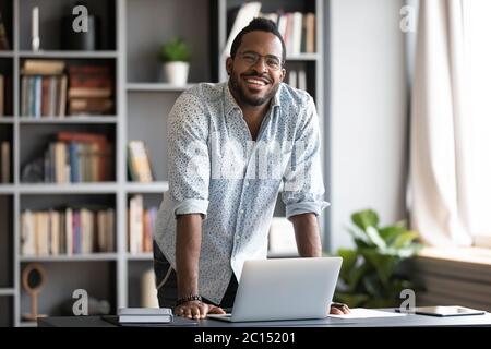 African man standing leaned over laptop smiling looking at camera Stock Photo