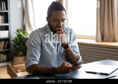 African guy holding smartphone feels concerned thinking over received message Stock Photo