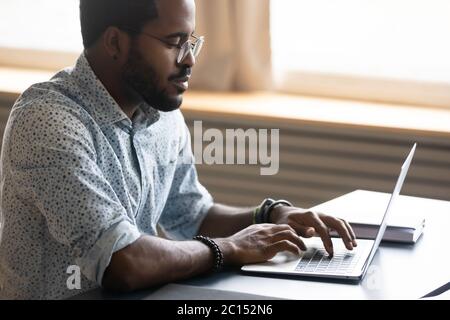 Focused african businessman working on laptop seated at desk Stock Photo