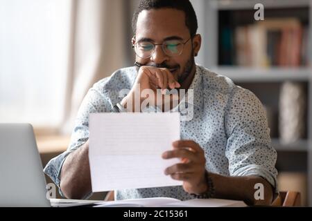 African man sitting at desk reading letter feels satisfied Stock Photo