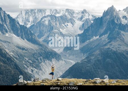 Young healthy man at sunny day practicing yoga at high altitude on beautiful Mont Blanc glacier background. Location place Nature Reserve Stock Photo