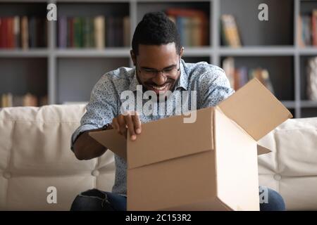 African guy opening parcel box seated on couch at home Stock Photo
