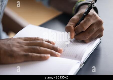 African man seated at desk writes information on notebook closeup Stock Photo