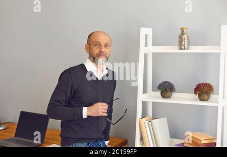 A middle-aged teacher professor with glasses in his hands at the workplace. Stock Photo