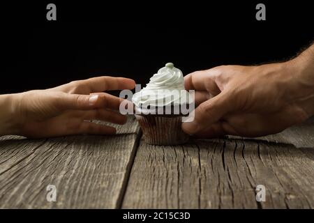 A chocolate cupcake topped with whipped cream. A male and a female hand are reaching out for a cupcake. Stock Photo