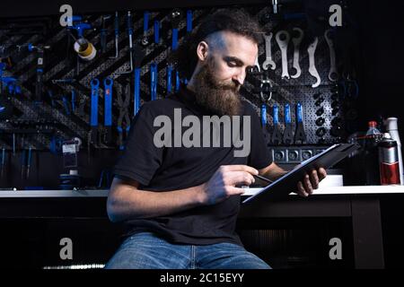 Stylish bicycle mechanic making notes in clipboard in workshop. theme small business selling, repair and service bicycles. Technician Doing Stock Photo