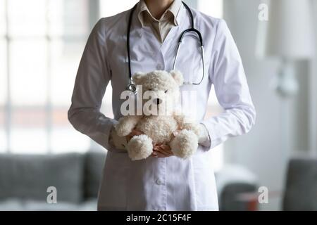 Close up young female pediatrician holding fluffy teddy toy Stock Photo