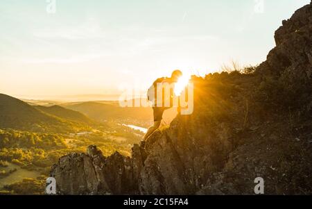 Travel man tourist alone on the edge cliff mountains and looking on the valley. Silhouette of the person on the high rock at sunset. Hiking adventure Stock Photo