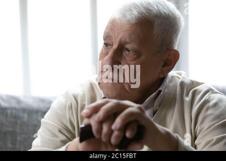 Close up thoughtful sad older man folded hands on cane Stock Photo