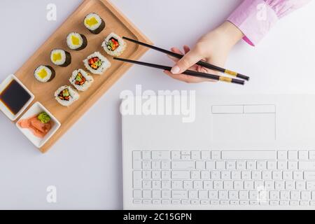 High angle view of businesswoman eating sushi next to her laptop. Take away japanese food and online order concept. Stock Photo