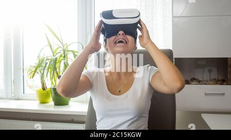 Portrait of smiling excited girl sitting at home and using VR goggles Stock Photo
