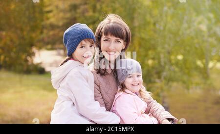 Youn woman with two daughters. Outdoors. Autumn background. Mother day Stock Photo