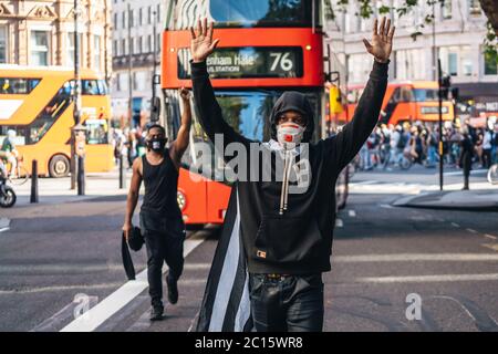 London / UK - 06/13/2020: Black Lives Matter protest during lockdown coronavirus pandemic. Man with American flag cape walking in front of the bus wit Stock Photo