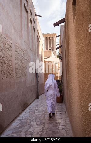 Dubai / United Arab Emirates - February 1, 2020: Muslim man in white traditional clothes walking in beautiful view of historical district Al Souq Al Kabeer of Dubai open for tourism Stock Photo