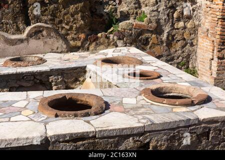 Roman Grande Taberna (fast food outlet) with marble covered counter and ceramic clayware containers in the ancient city of Herculaneum, Italy Stock Photo