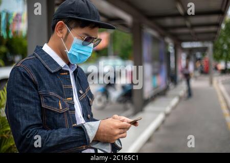 Asian Young man using smart phone in the city and wearing face mask for protection air pollution, particulates and for protection flu virus, influenza Stock Photo