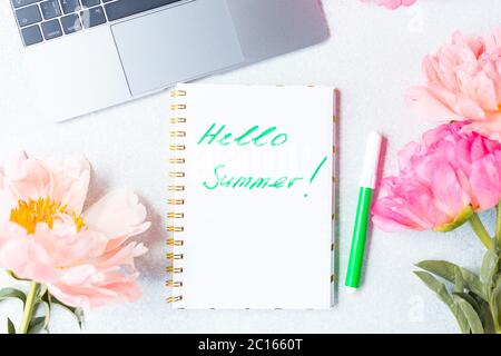 Desk top view. Phrase words Hello Summer. Peonies top view, flat lay. Peony flowers and laptop. Good morning.  Stock Photo