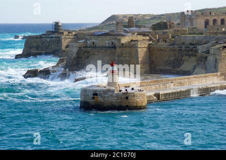 VALLETTA, MALTA - DEC 31st, 2019: View from Fort St Elmo on to the Ricasoli Grand Harbour East Breakwater and red lighthouse during strong waves Stock Photo