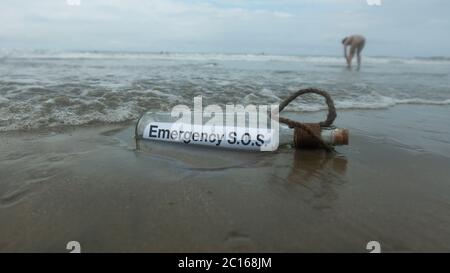 Emergency SOS Pollution message inside the glass bottle dragged by the abandoned tide on the beach buried in the sand Stock Photo