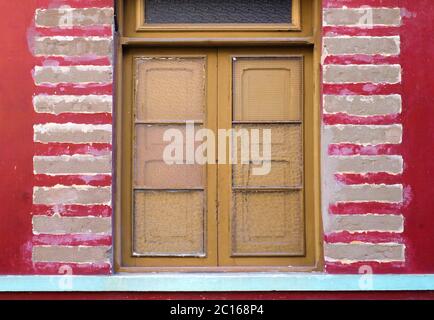 Shuttered window frame with broken glass and red wall sections, old derelct and abandoned house detail in Latino architecture style. Stock Photo